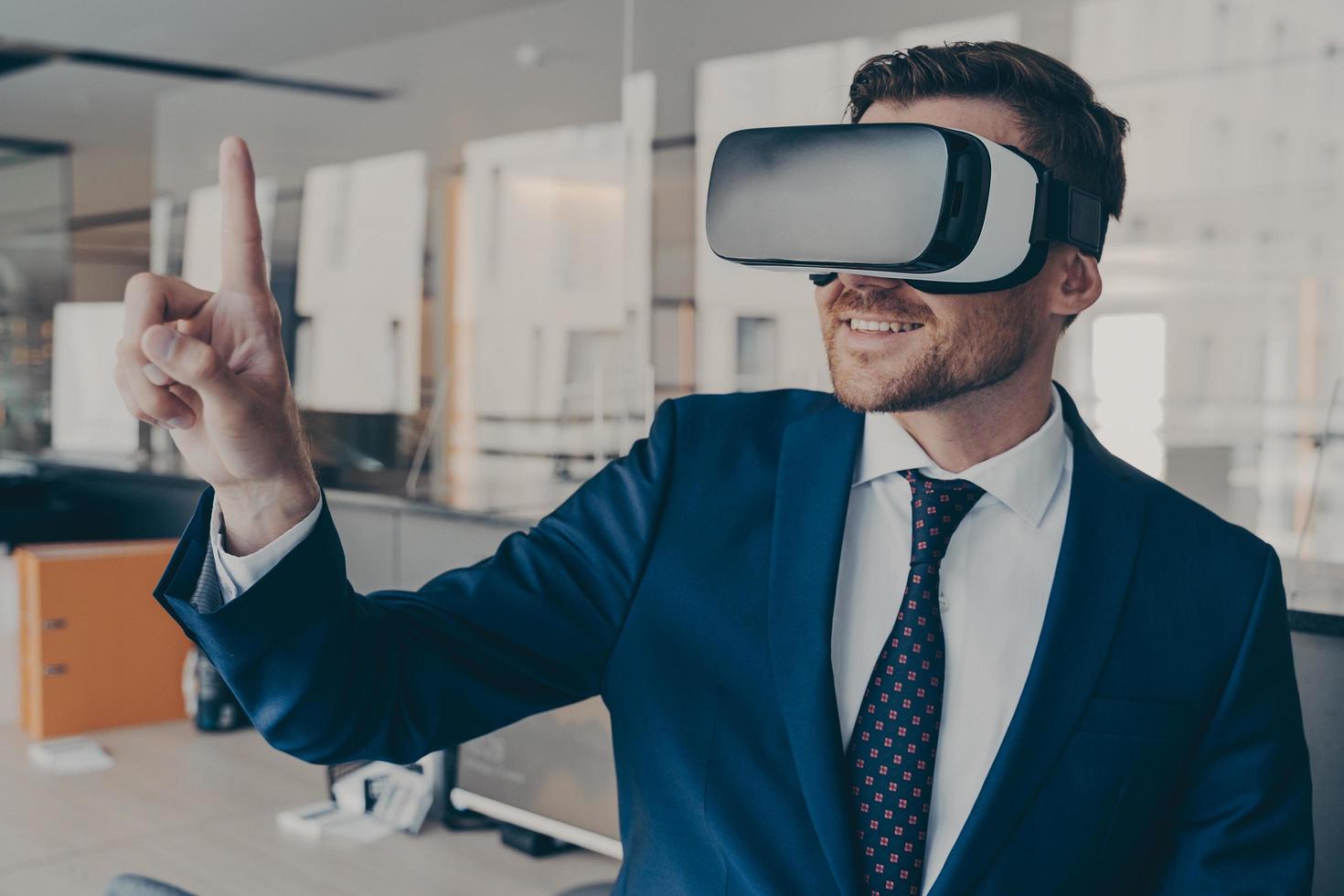 Young financier wearing VR headset glasses, while standing in his office photo