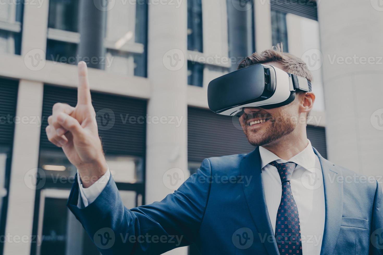 Smiling bearded businessman with stubble wearing VR glasses, viewing something in virtual reality photo