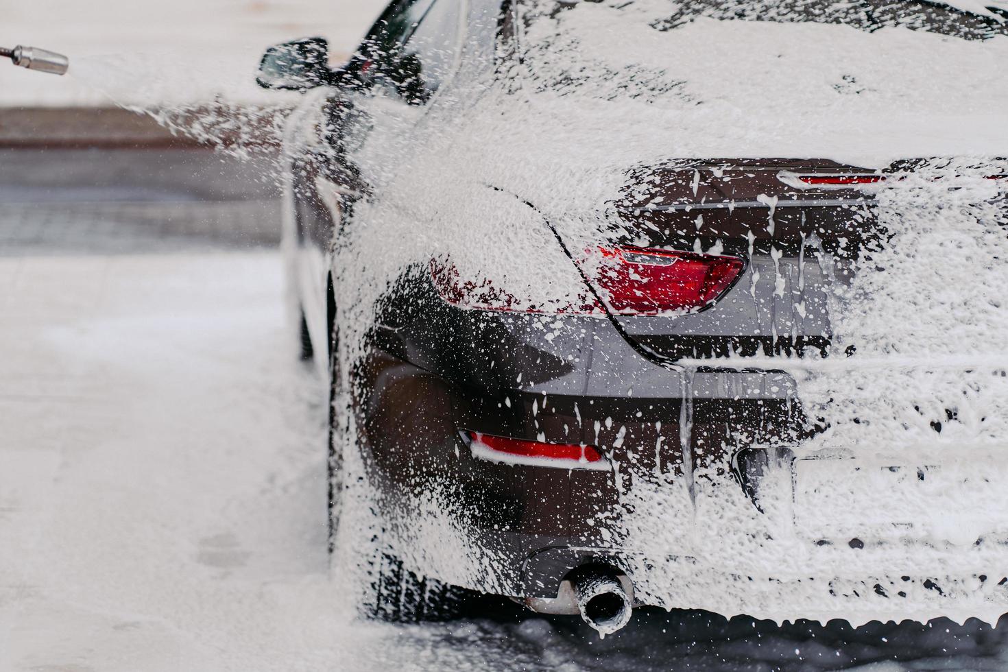 Horizontal shot of car covered with soap foam. Cleaning service. Water pressure on automobile. Manual car washing. High pressure cleaning photo