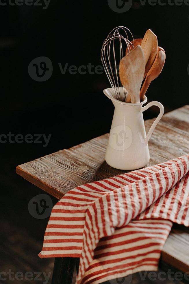 Vertical shot of vintage kitchen utensils in white ceramic jar on wooden table. Home kitchen decor. Kitchenware for cooking. Household items photo