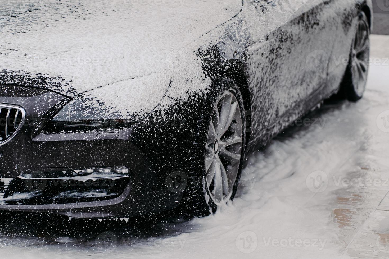 Horizontal shot of black automobile covered with bubble soap foam at carwash. Detail cleaning. Purifying concept photo