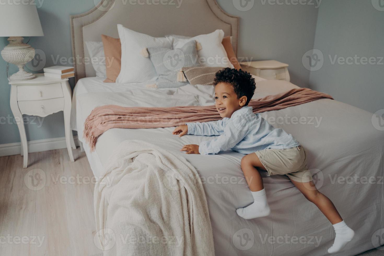 Joyous little african american kid enjoying playtime indoors on bed photo
