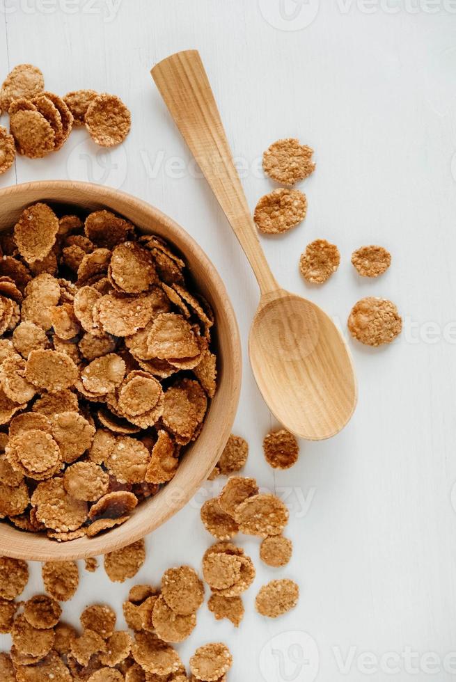 Crispy healthy dry cereal flakes in a wooden bowl with wooden spoon on white background photo