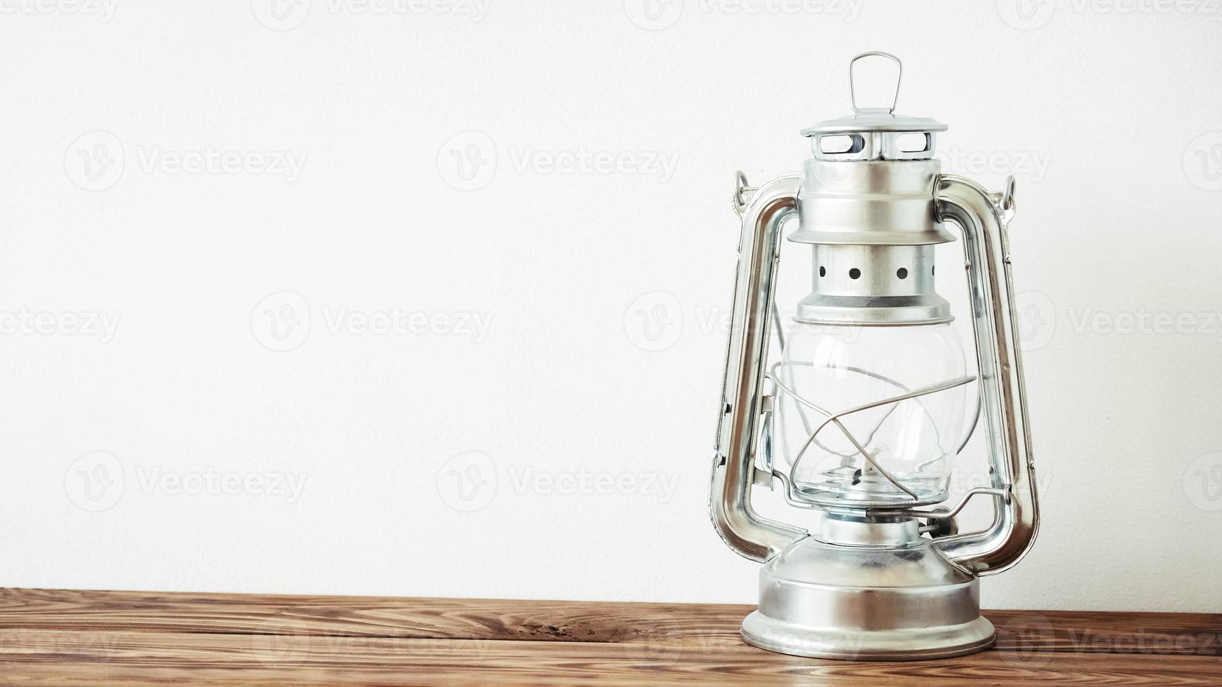 Vintage kerosene lamp on wooden table over white wall background photo