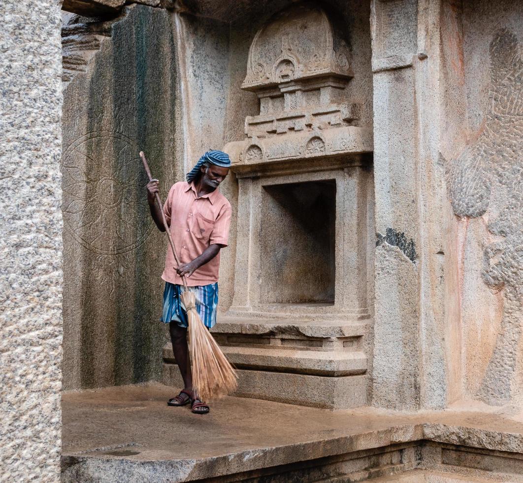 Mamallapuram, Tamil Nadu, India - August 2018 An old Indian sweeper cleans the floor of the ancient Pallava caves in Mahabalipuram with a wooden broom. photo