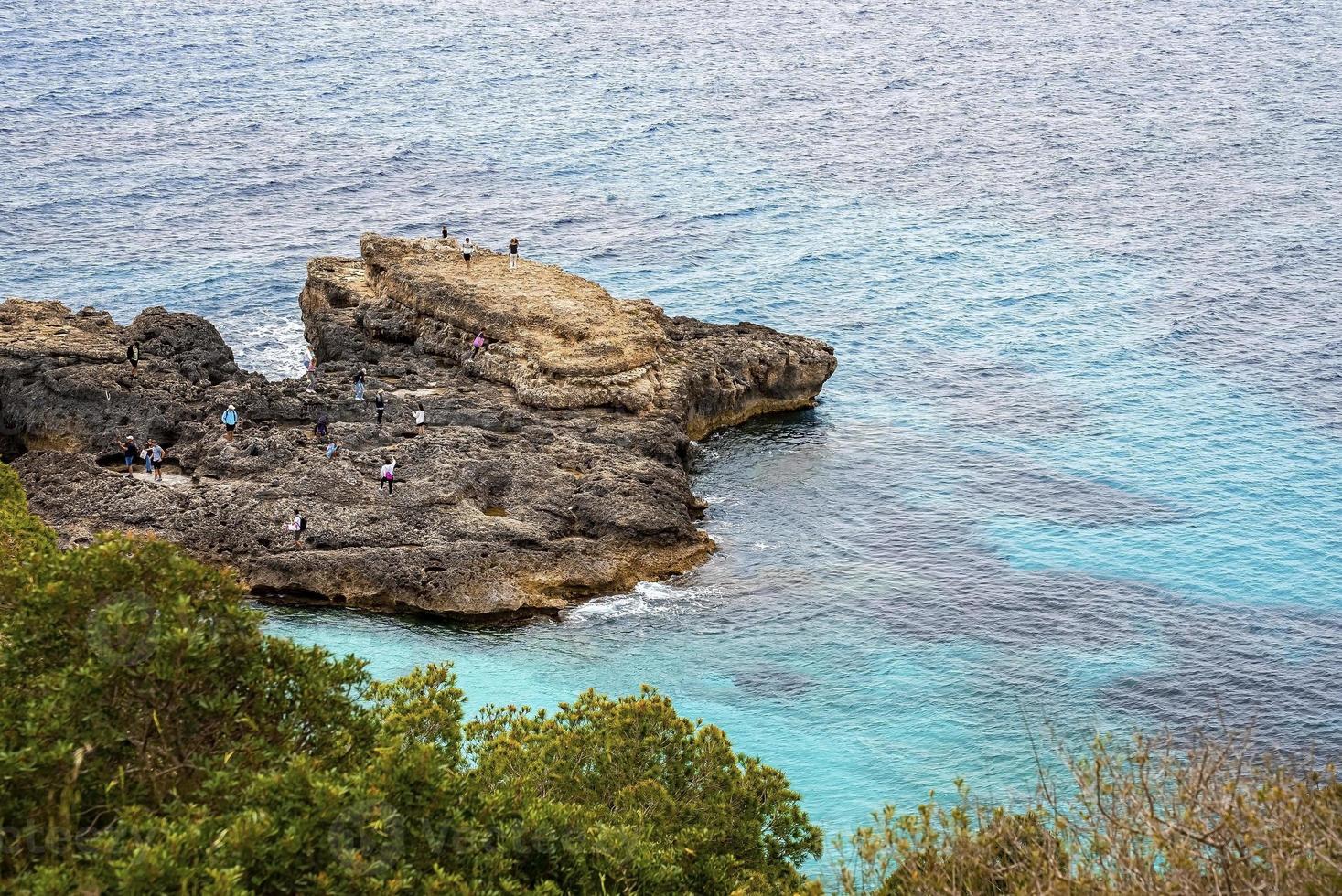 vista de ángulo alto de los turistas que exploran el acantilado rocoso por mar en la isla escénica foto