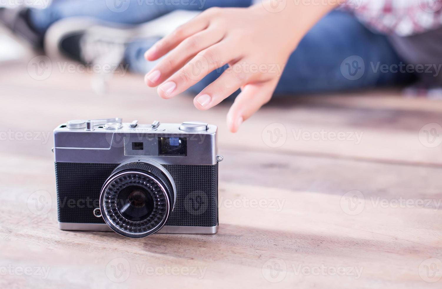 joven fotógrafa hipster tomando fotos y mirando la cámara sentada en el suelo de madera.