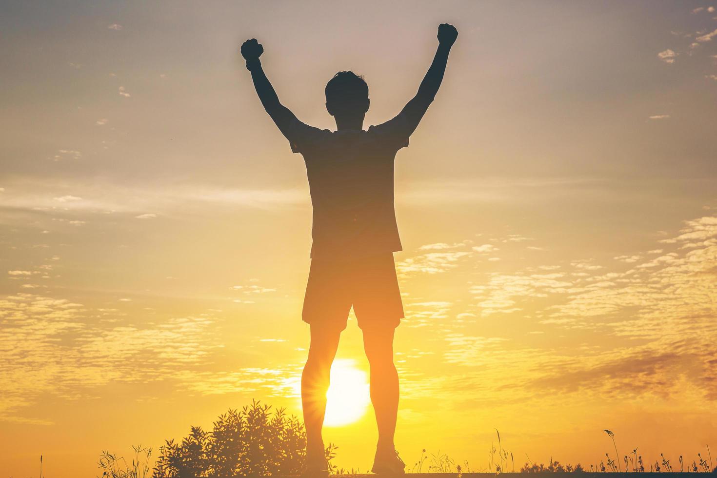 Silhouette of male runner standing and open arm celebrate their success with healthy at the road track with sunset background. photo