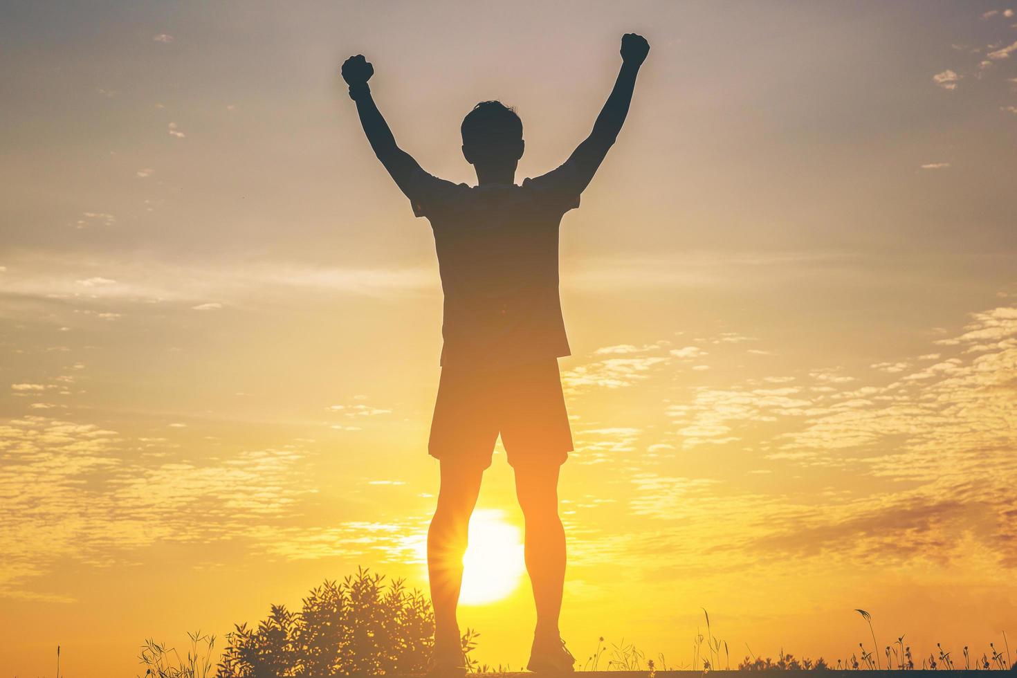 silueta de corredor masculino de pie y brazo abierto celebra su éxito con salud en la pista de carretera con fondo de puesta de sol. foto