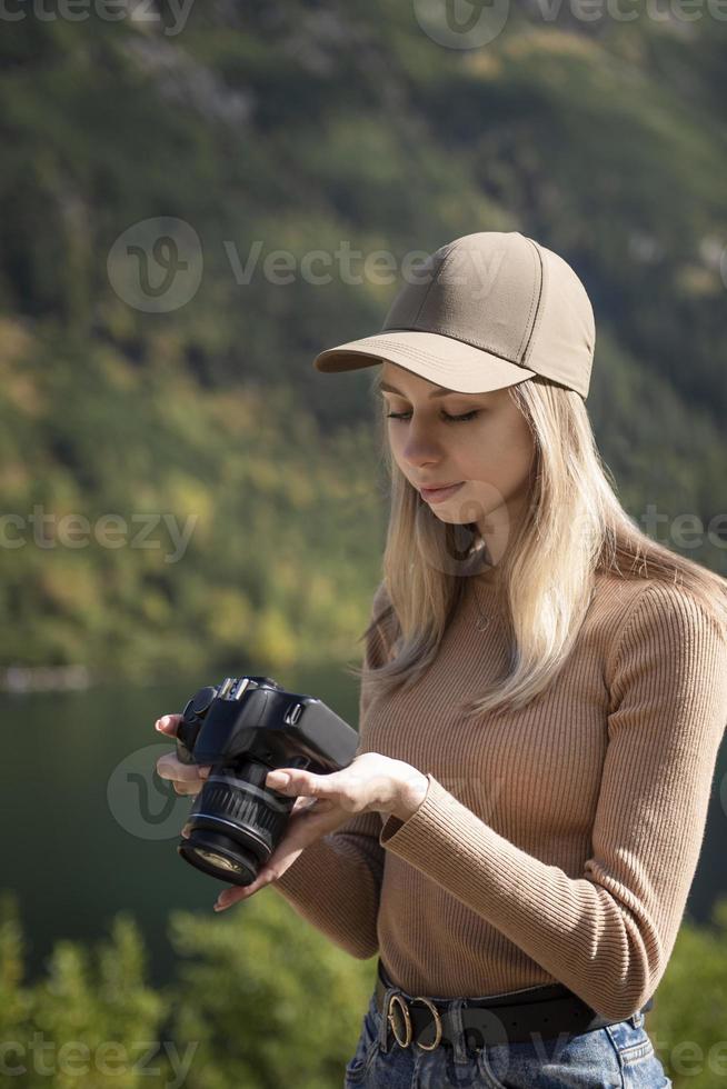 Photographer tourist traveler standing on green top on mountain holding in hands digital photo camera