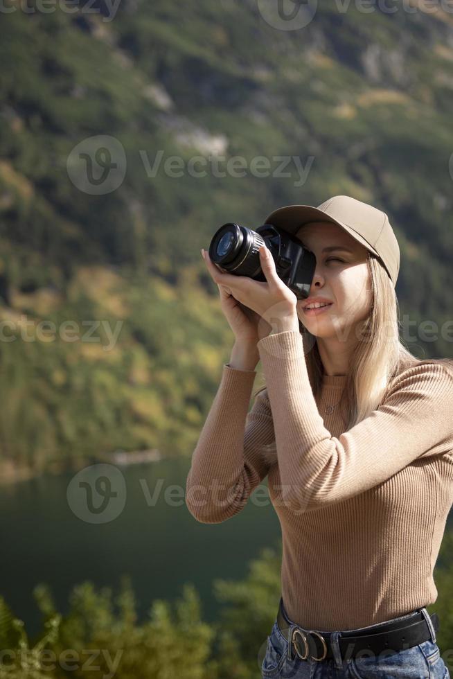 Photographer tourist traveler standing on green top on mountain holding in hands digital photo camera