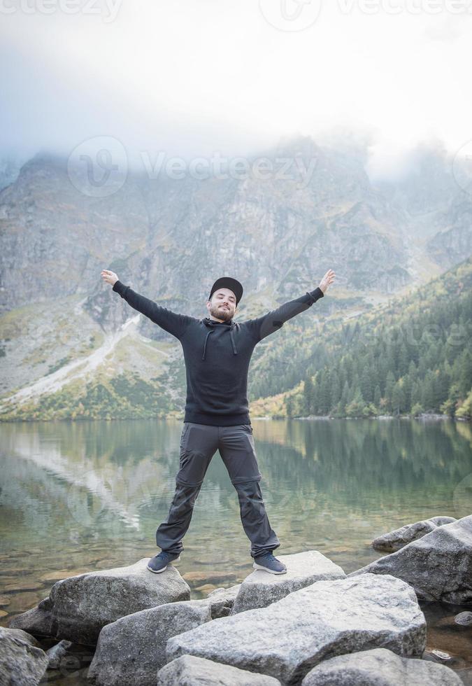 Young tourist man in a cap with hands up on the top of the mountains photo