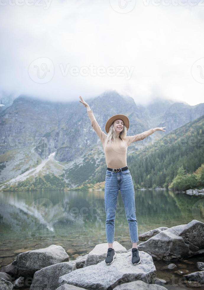 Young tourist woman in a hat with hands up on the top of the mountains photo