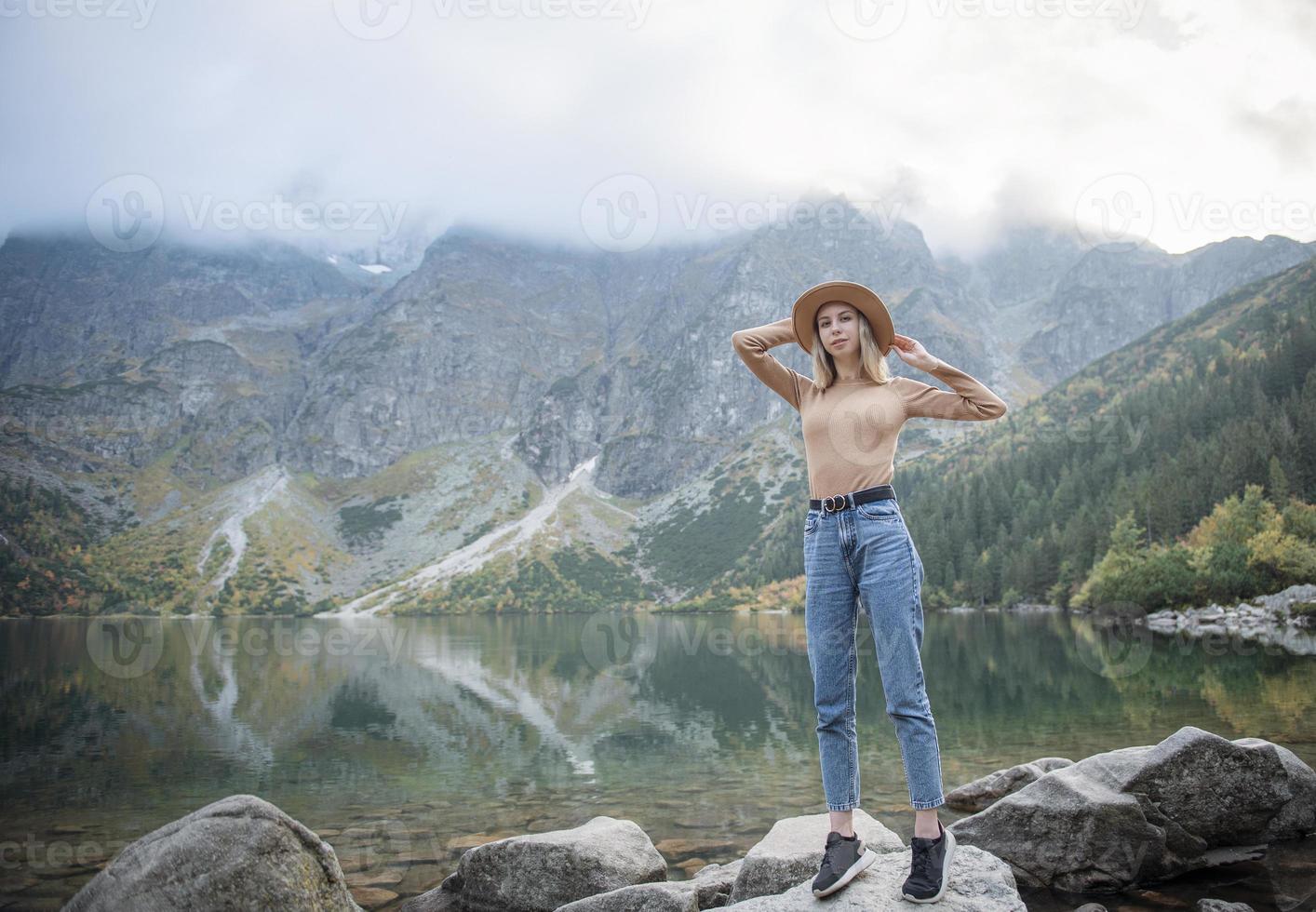 Young tourist woman in a hat with hands up on the top of the mountains photo