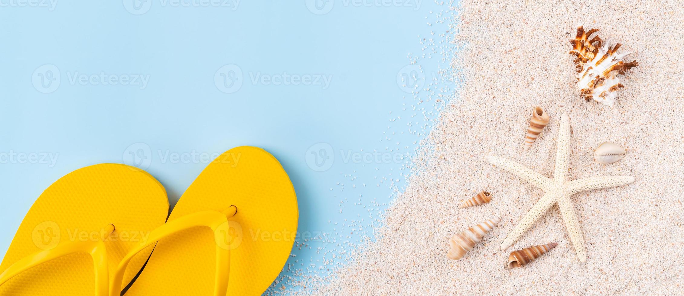 Top view with copy space of yellow sandals with starfish and shells, sand on blue background. photo