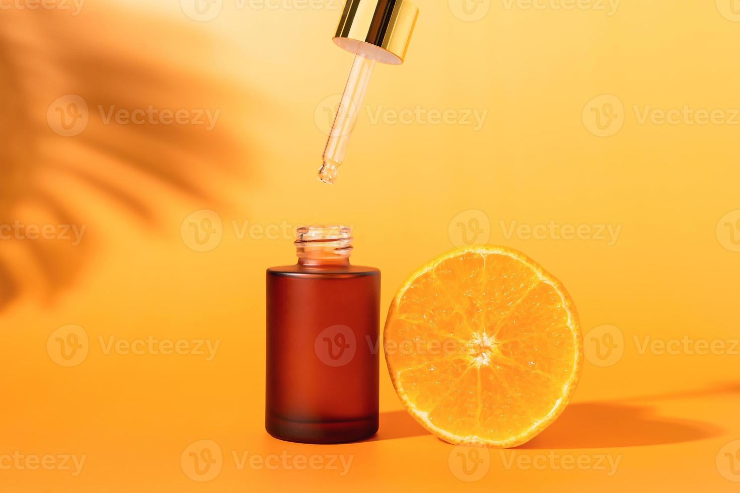 botella de suero con cuentagotas y rodaja de naranja, ingredientes para el cuidado de la piel y tratamiento de vitamina sobre fondo blanco, concepto de cosmética natural. foto