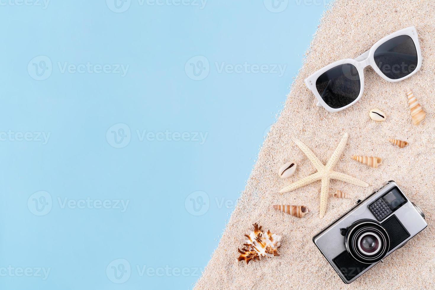 Top view with copy space of camera and sunglasses and starfish, shells with sand on blue background. Summer time concept. photo