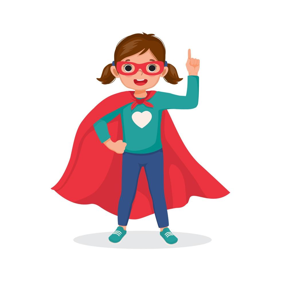 Cute little girl playing dressed in superhero costume standing with hand on hip pose pointing index finger up vector