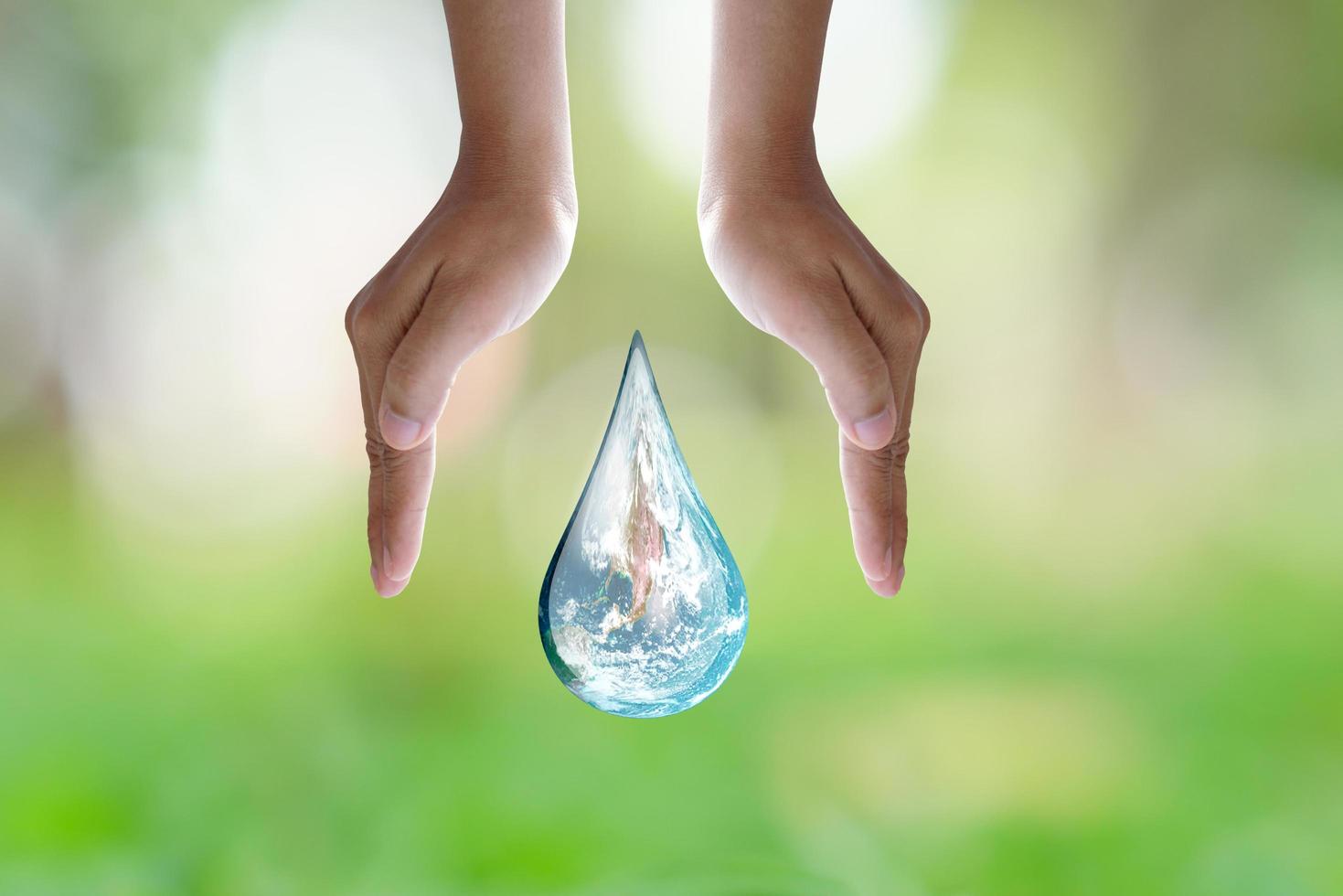 día mundial del medio ambiente. mano humana que protege la gota de agua con luz solar sobre fondo verde de la naturaleza. foto