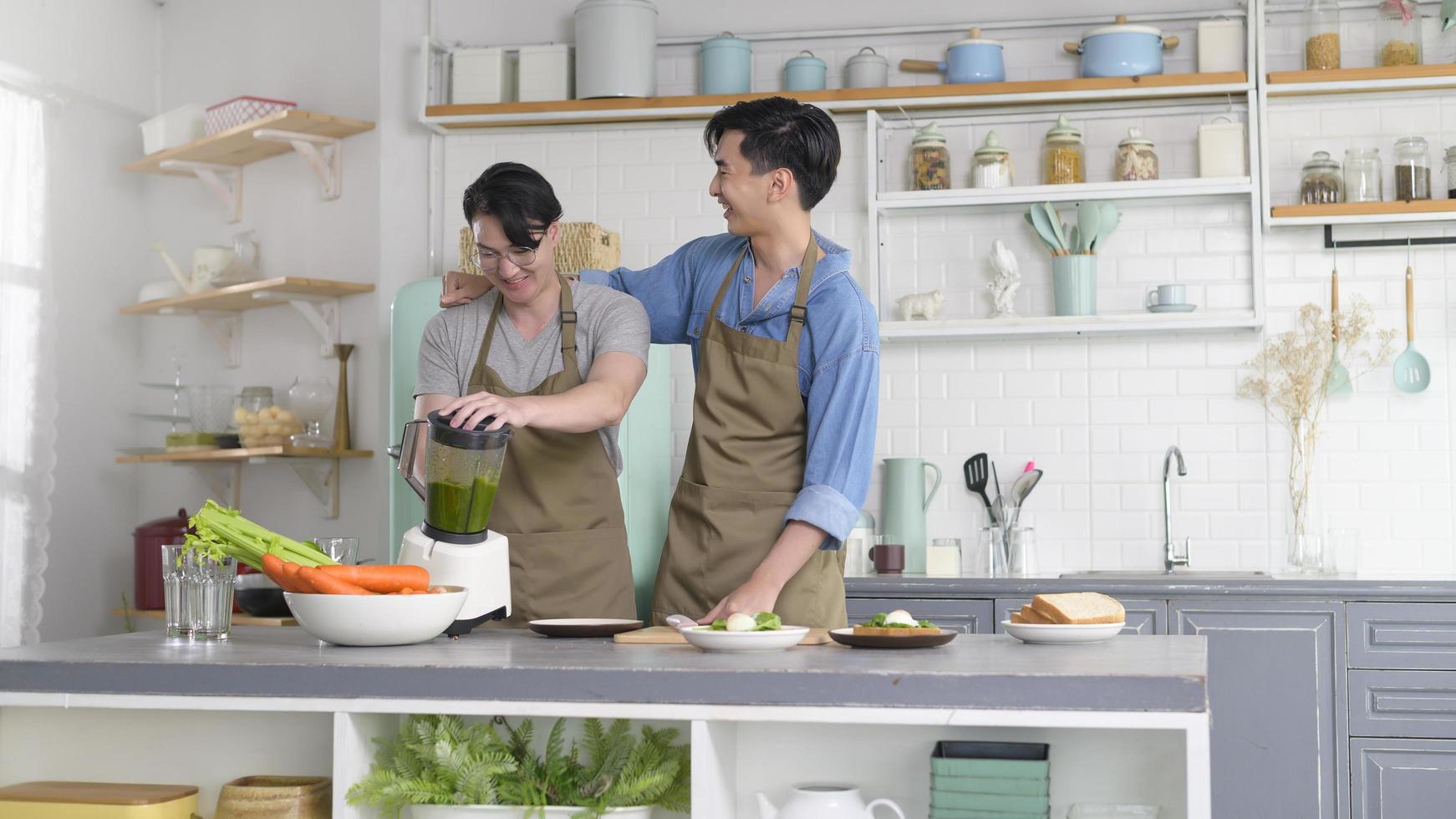 Young smiling gay couple making healthy juice with juice machine in the kitchen at home, LGBTQ and diversity concept. photo