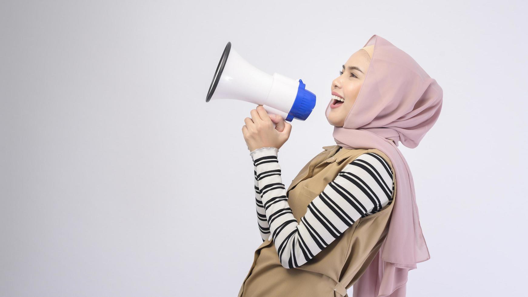 Happy muslim woman is announcing with megaphone on white background photo