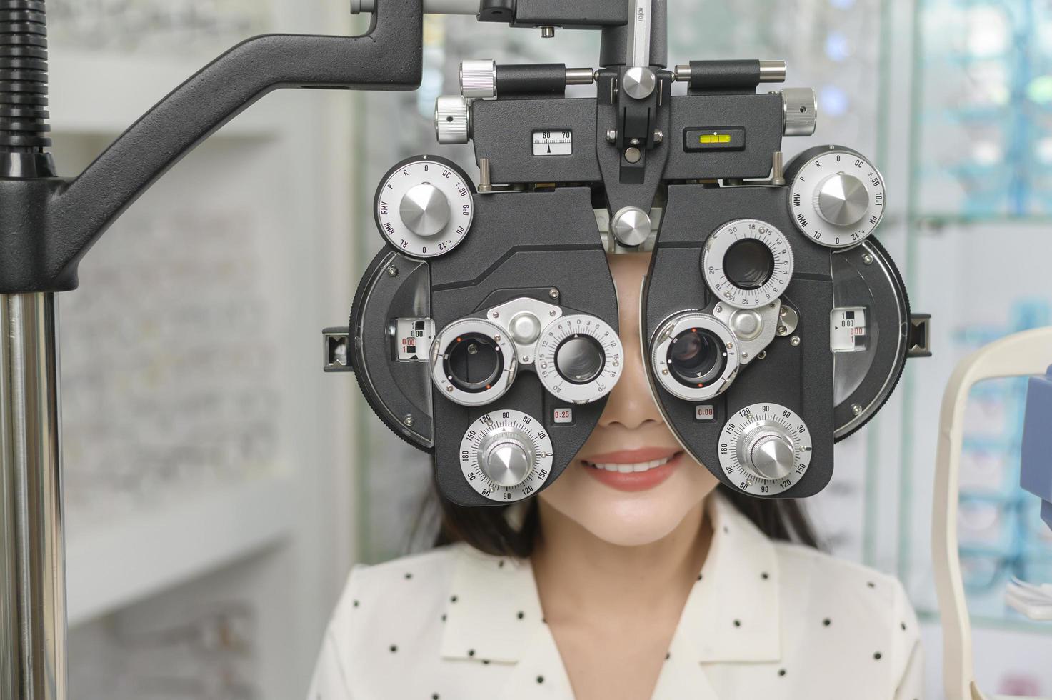 una joven clienta que está siendo examinada con una prueba visual usando un dispositivo de medición de la vista de optometría bifocal por un oftalmólogo en el centro óptico, concepto de cuidado de los ojos. foto