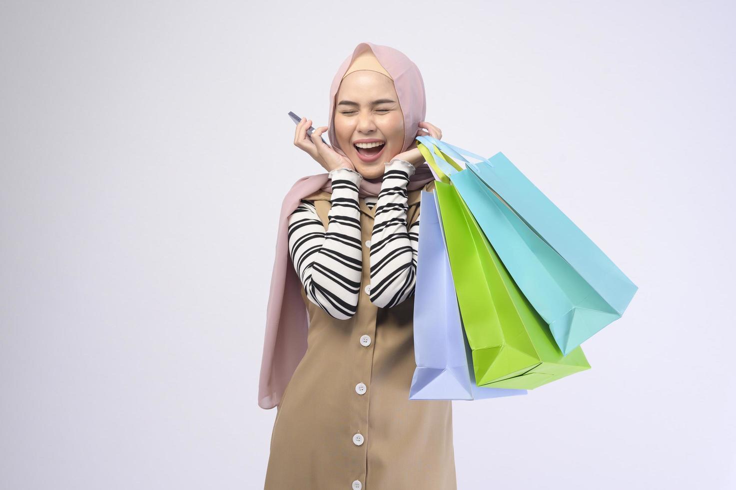 Young beautiful muslim woman in suit holding colorful shopping bags over white background studio photo