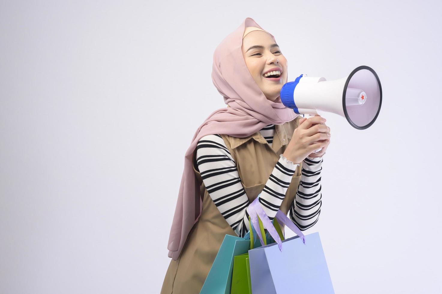 Young beautiful muslim woman in suit holding colorful shopping bags over white background studio photo