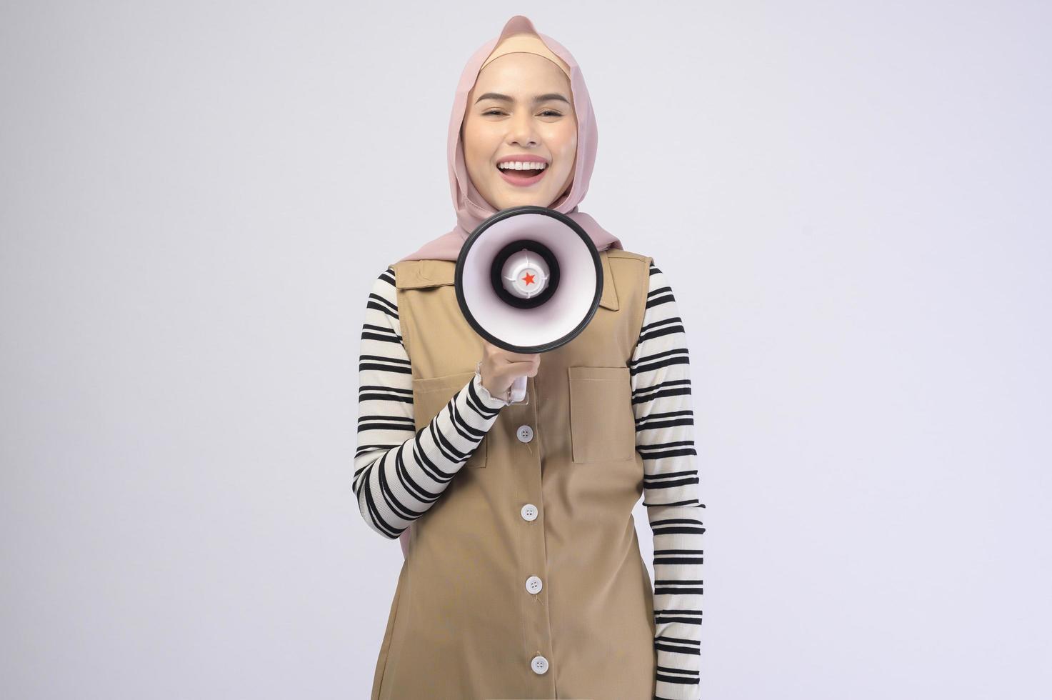 Happy muslim woman is announcing with megaphone on white background photo