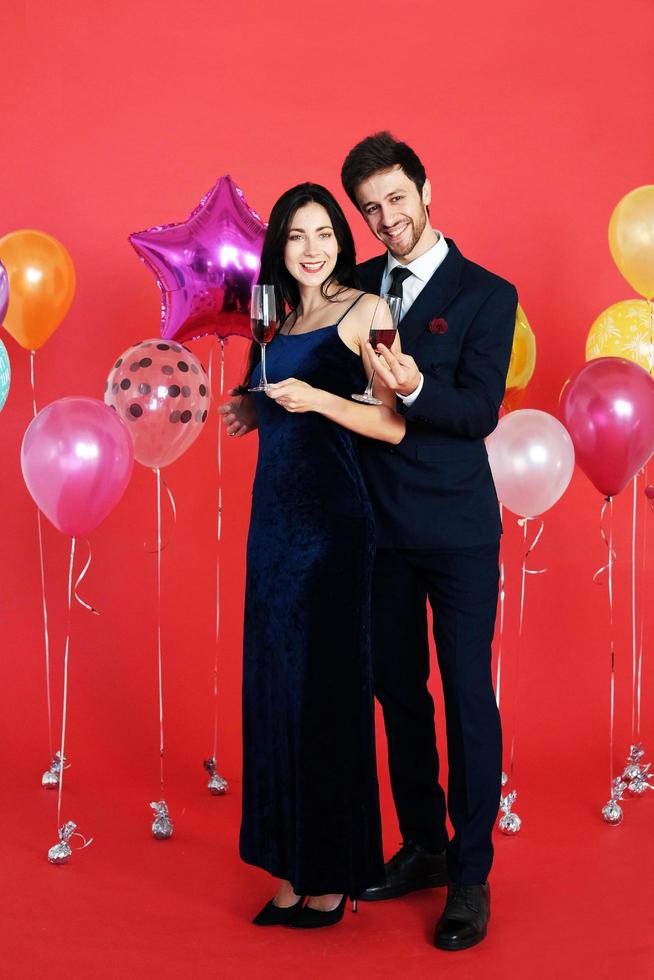 dulce pareja amor sonrisa y pasar romántico bebiendo vino en navidad y celebrando la víspera de año nuevo, día de san valentín con globo colorido sobre fondo rojo foto