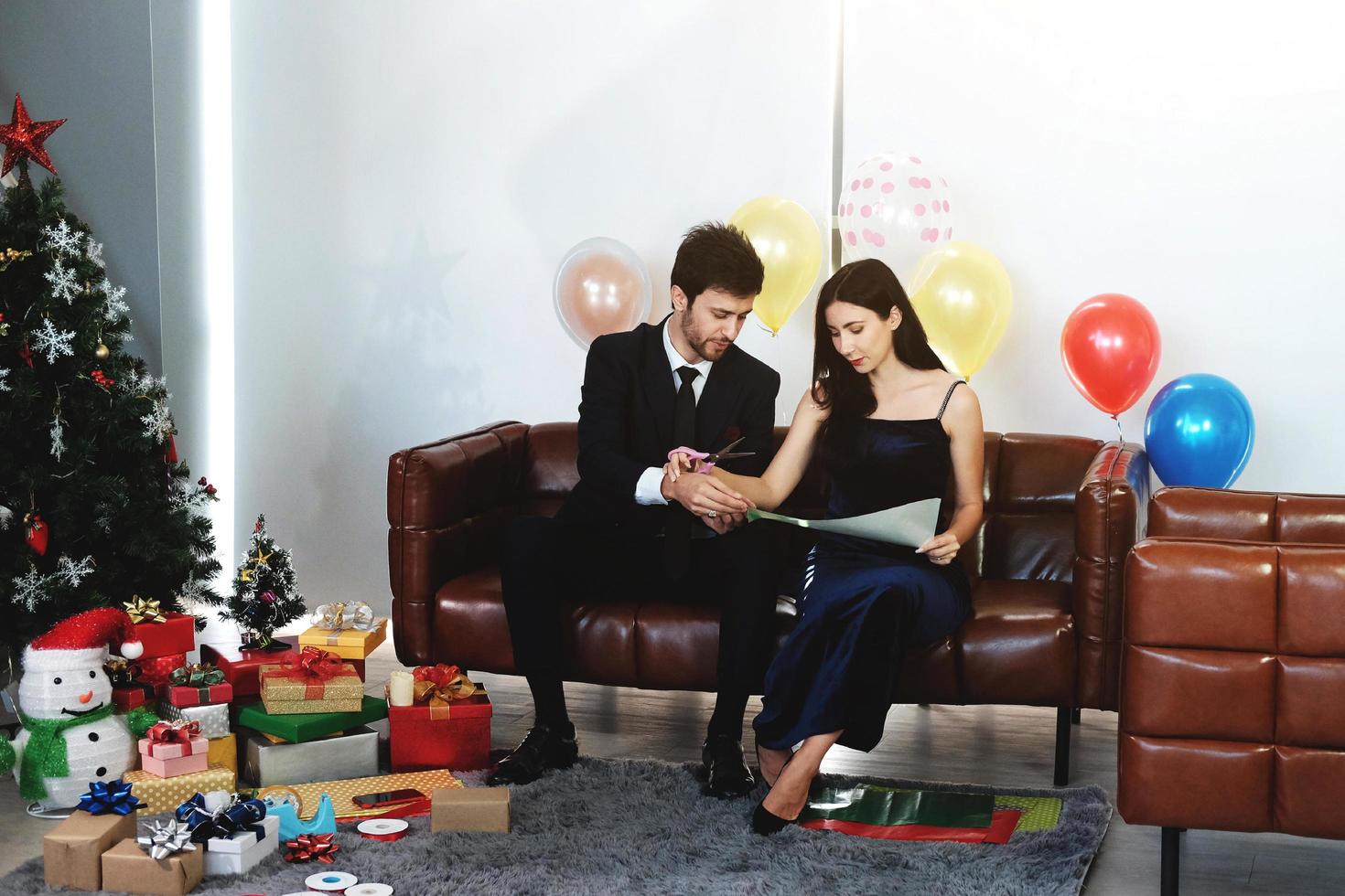 dulce pareja ama sonreír y pasar un tiempo romántico de navidad y celebrar la víspera de año nuevo en la decoración de un sofá marrón con árbol de navidad, globos coloridos y cajas de regalo en la sala de estar en casa foto