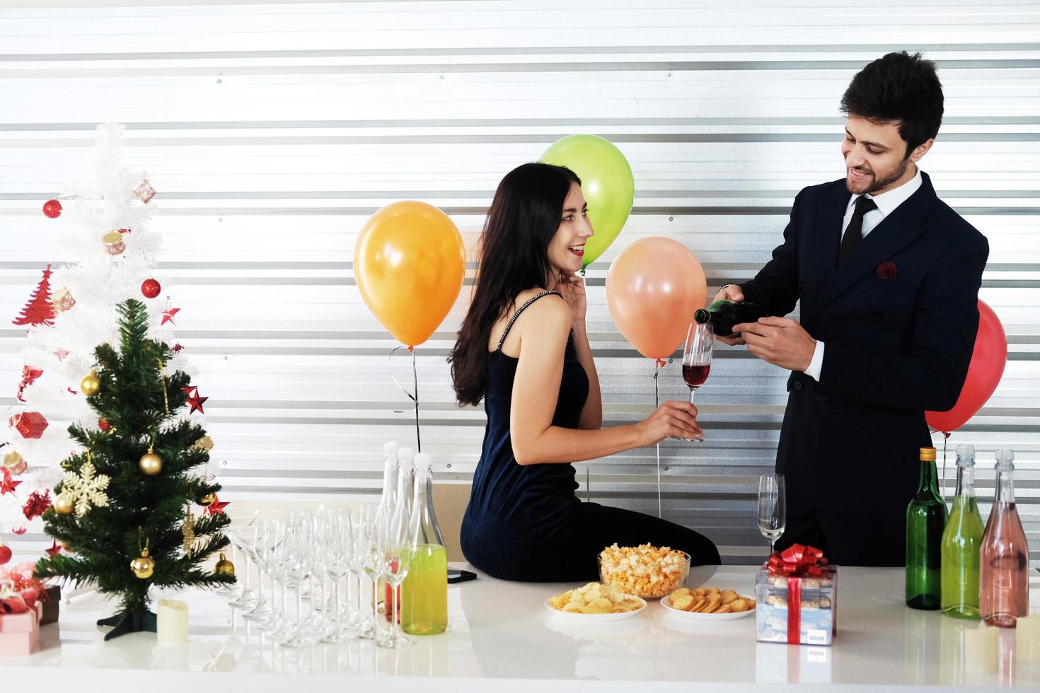 dulce pareja amor sonrisa y pasar romántico bebiendo vino en navidad y celebrando la víspera de año nuevo, día de san valentín con globos coloridos y cajas de regalo en el área de la despensa foto