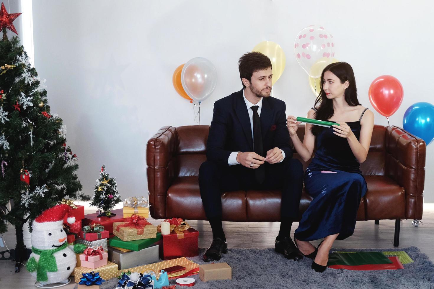 dulce pareja ama sonreír y pasar un tiempo romántico de navidad y celebrar la víspera de año nuevo en la decoración de un sofá marrón con árbol de navidad, globos coloridos y cajas de regalo en la sala de estar en casa foto