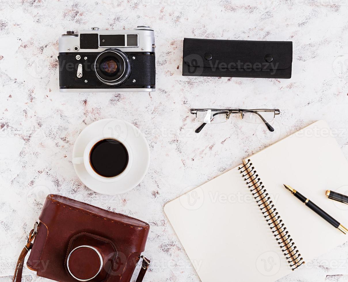 Flat lay, top view office table desk. Desk workspace with retro camera, diary, pen, glasses, case, cup of coffee on white background. photo