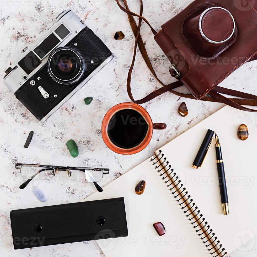 escritorio plano de oficina con vista superior. espacio de trabajo de escritorio con cámara retro, diario, bolígrafo, gafas, estuche, taza de café sobre fondo blanco. foto