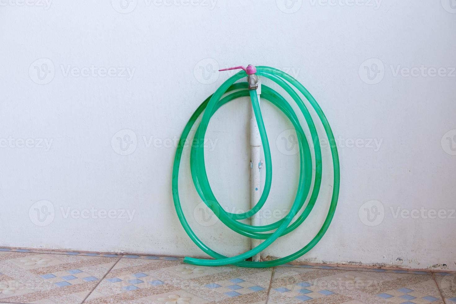 The roll of rubber watering hose is hanging on the faucet near the white wall. photo