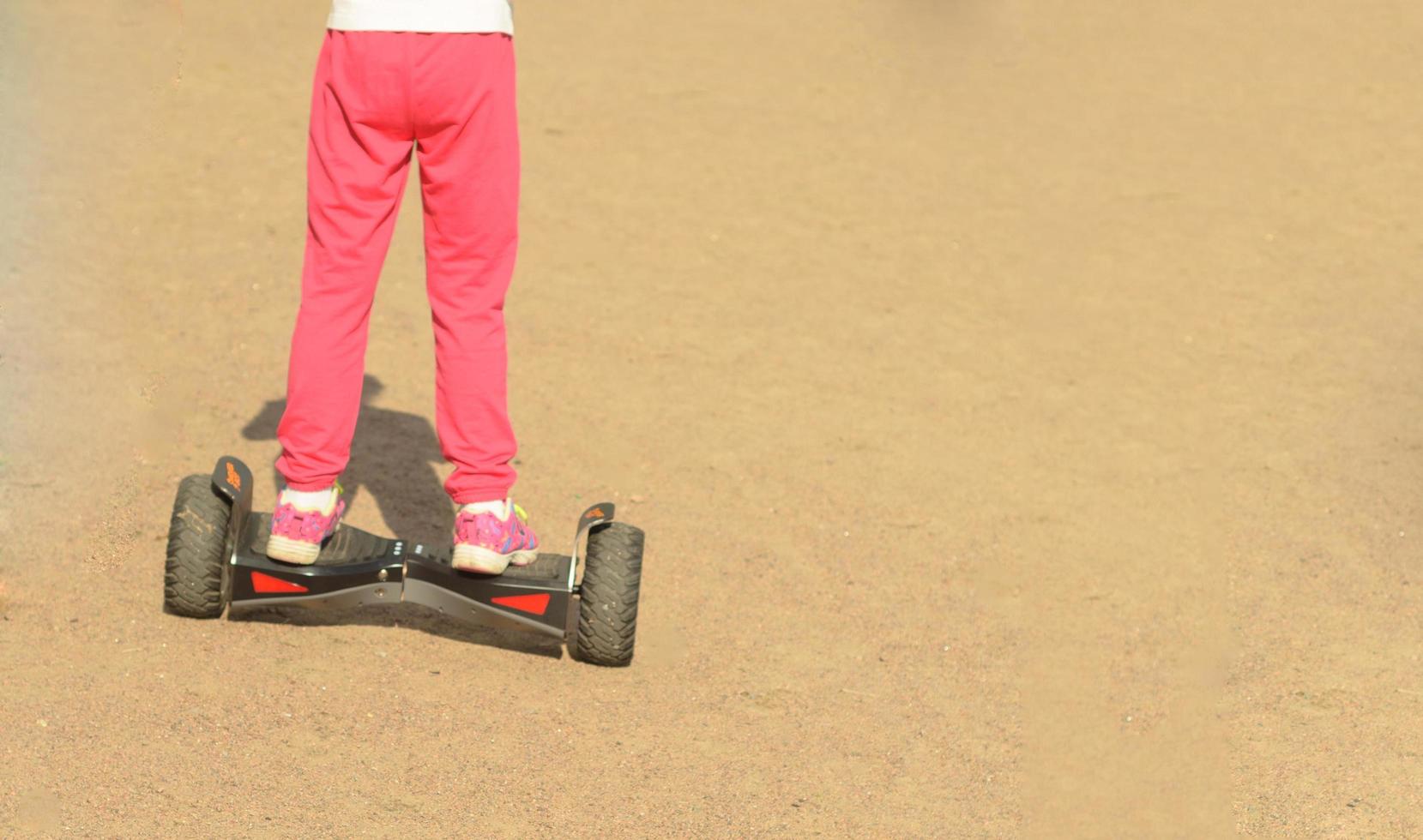 Small girl is driving on electric self-balancing scooter at sunny day.Walking on segway on sand. photo