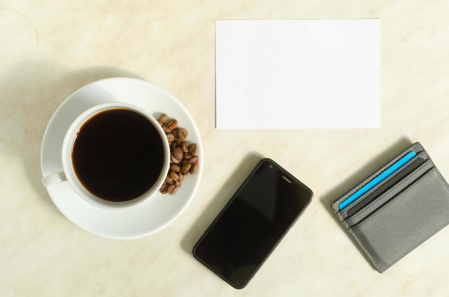 A cup of coffee with coffee beans, mobile phone, bank cards and empty blank on the table. photo