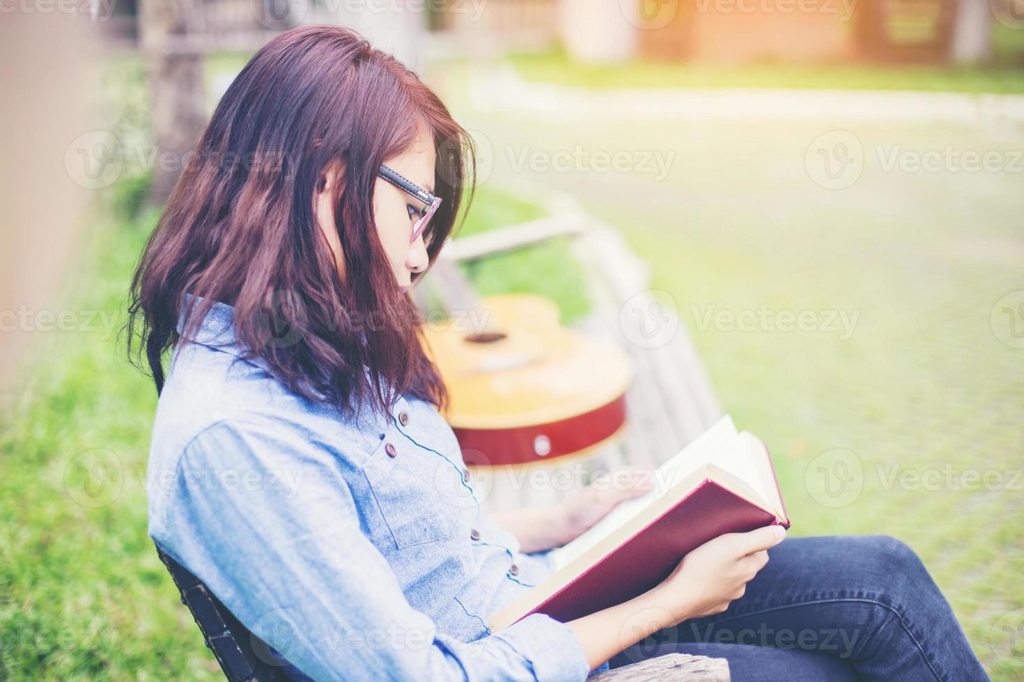 chica encantadora hipster relajándose en el parque mientras lee un libro, disfruta de la naturaleza. foto