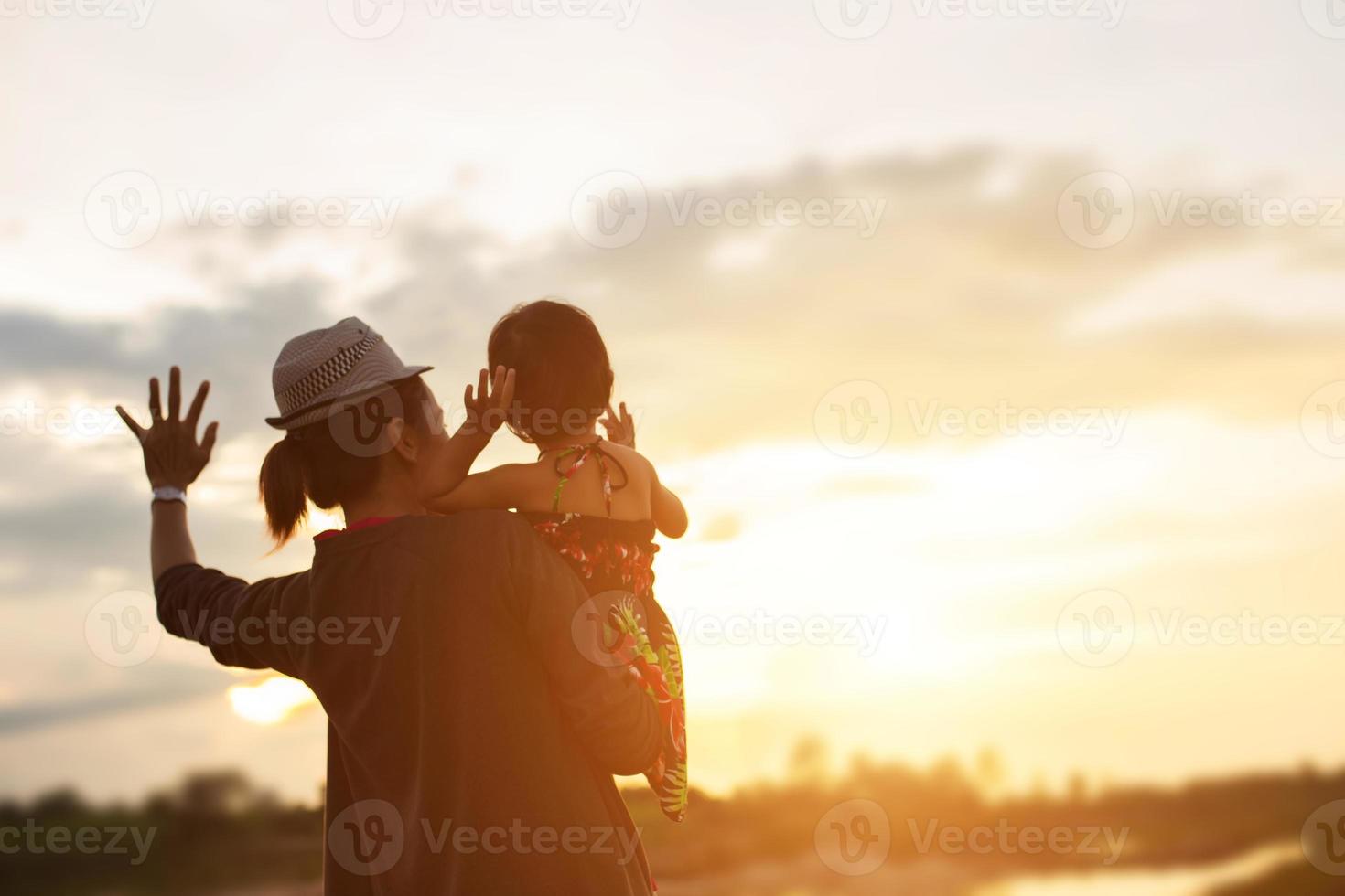 a silhouette of a happy young girl child the arms of his loving mother for a hug, in front of the sunset in the sky on a summer day. photo