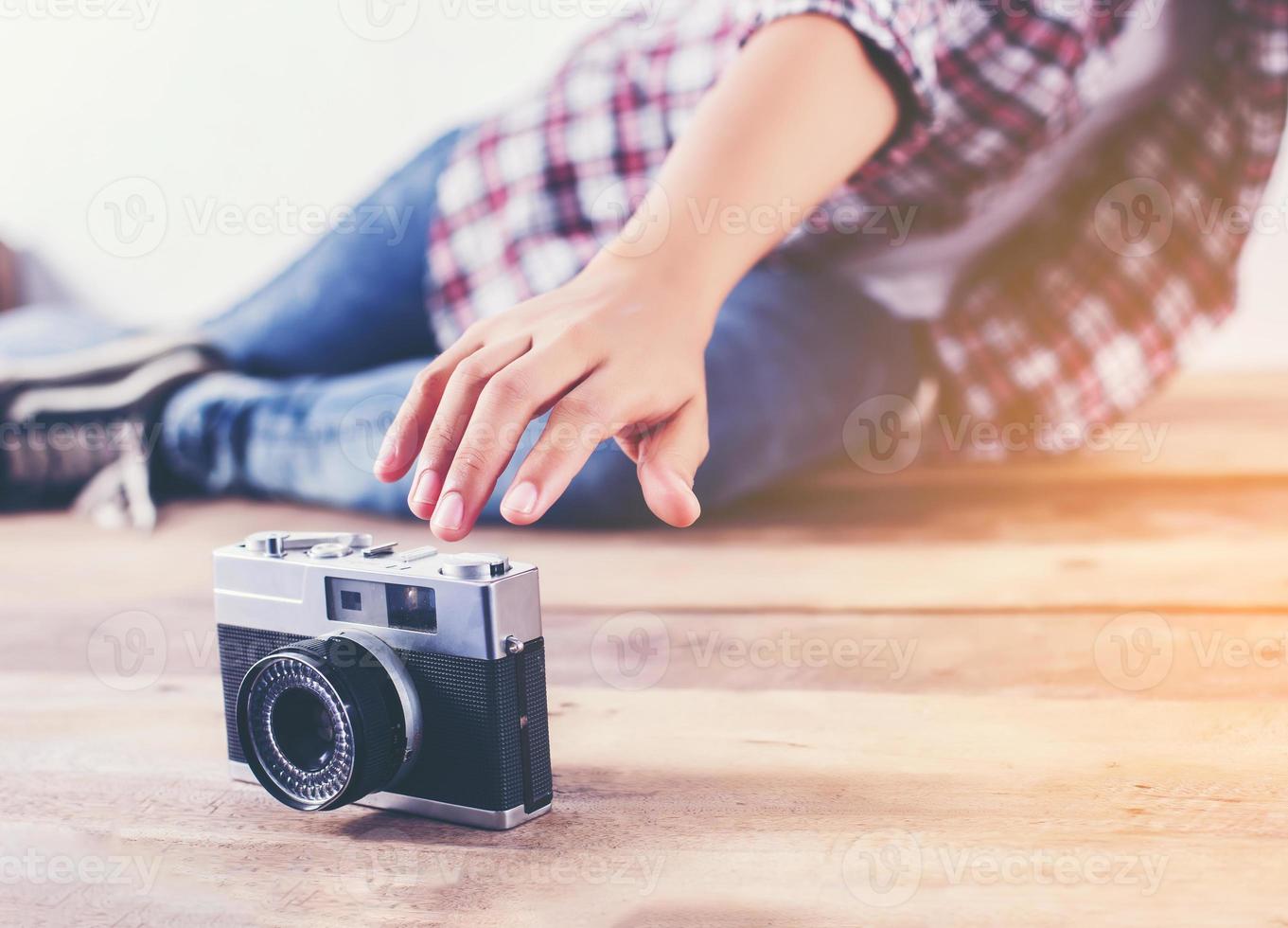 Young hipster photographer woman taking photo and look at camera sitting on wooden floor.