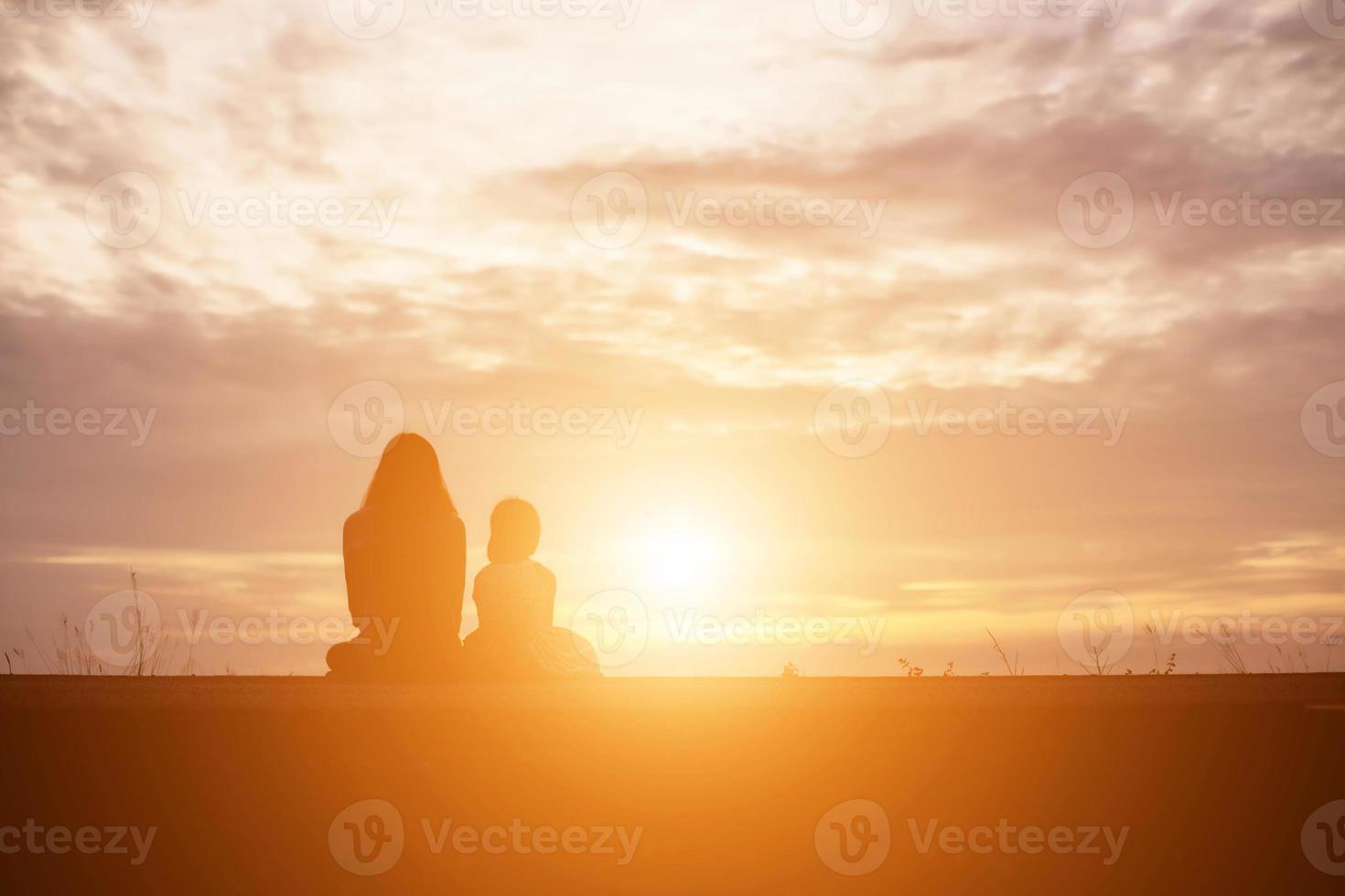 a silhouette of a happy young girl child the arms of his loving mother for a hug, in front of the sunset in the sky on a summer day. photo