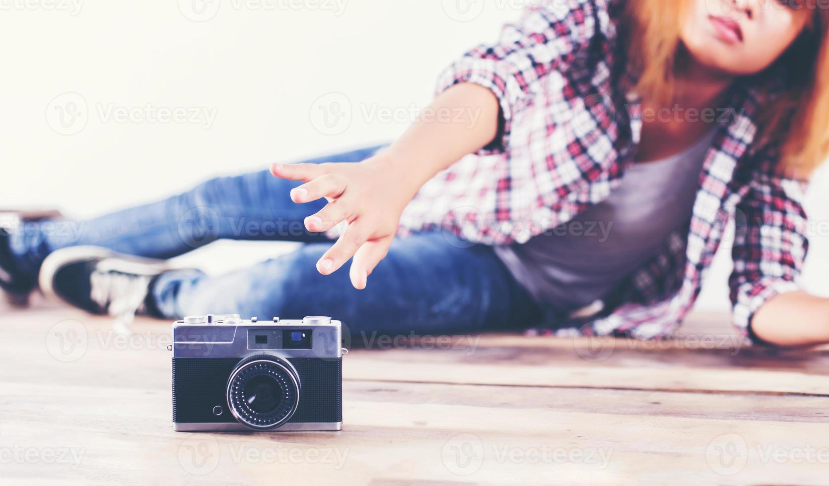 joven fotógrafa hipster tomando fotos y mirando la cámara sentada en el suelo de madera.