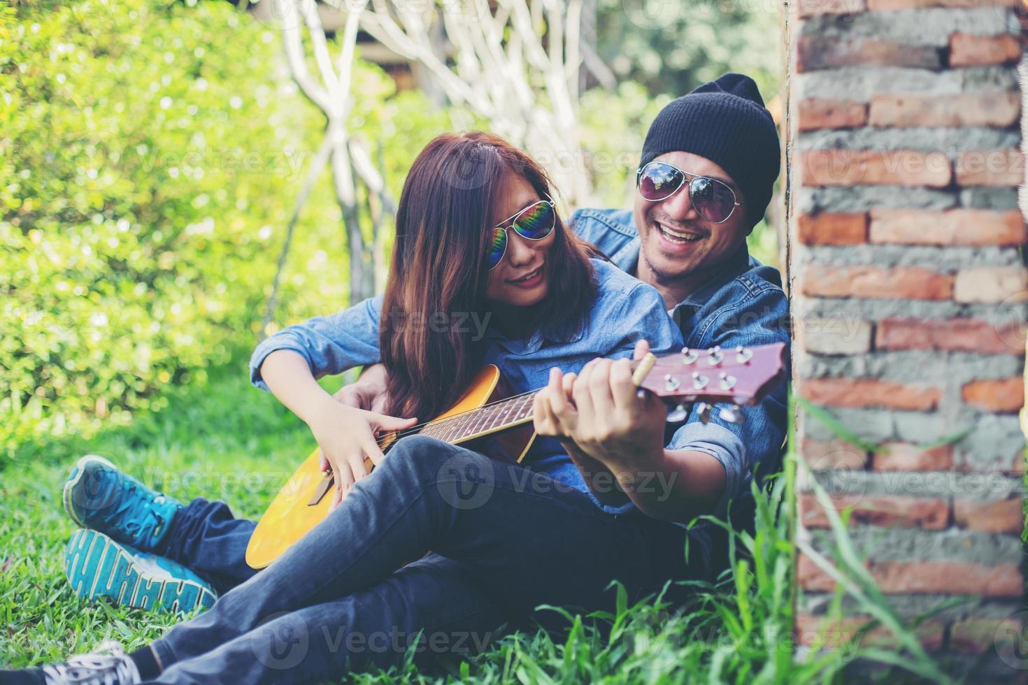 Hipster man playing guitar for his girlfriend outdoor against brick wall, enjoying together. photo