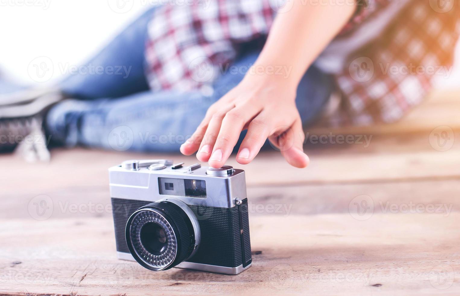 Young hipster photographer woman taking photo and look at camera sitting on wooden floor.