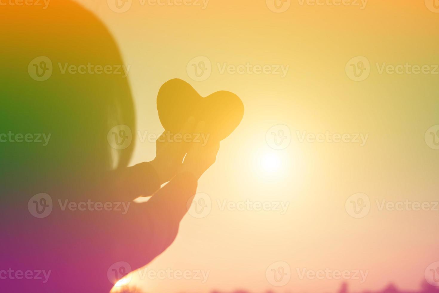 hands forming a heart shape with sunset silhouette photo