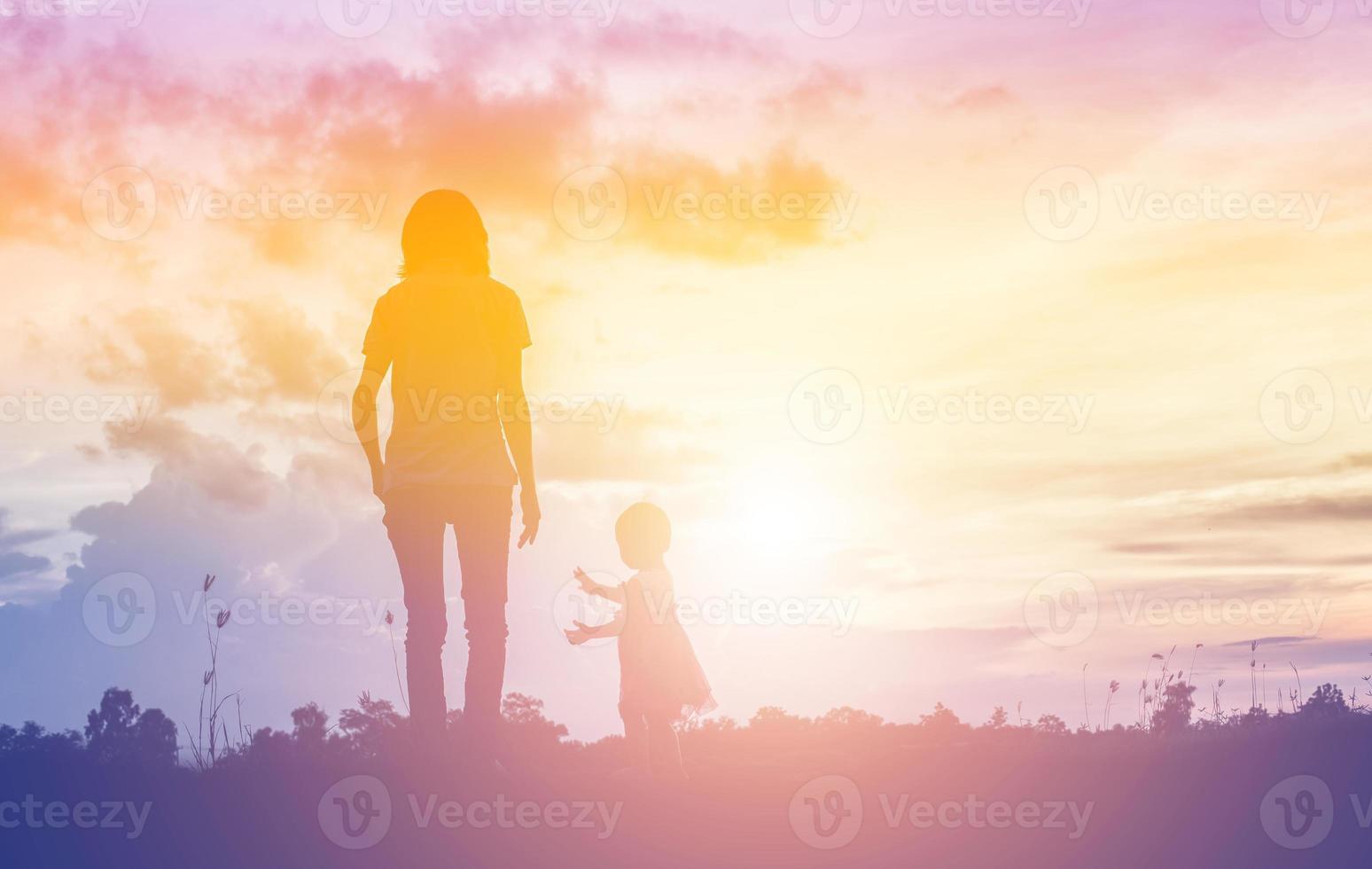 a silhouette of a happy young girl child the arms of his loving mother for a hug, in front of the sunset in the sky on a summer day. photo