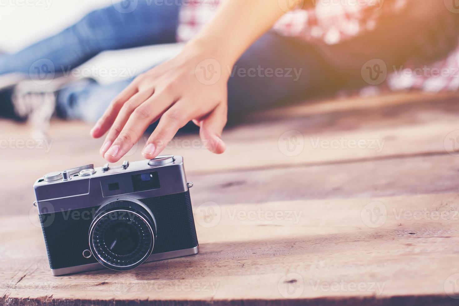 Young hipster photographer woman taking photo and look at camera sitting on wooden floor.