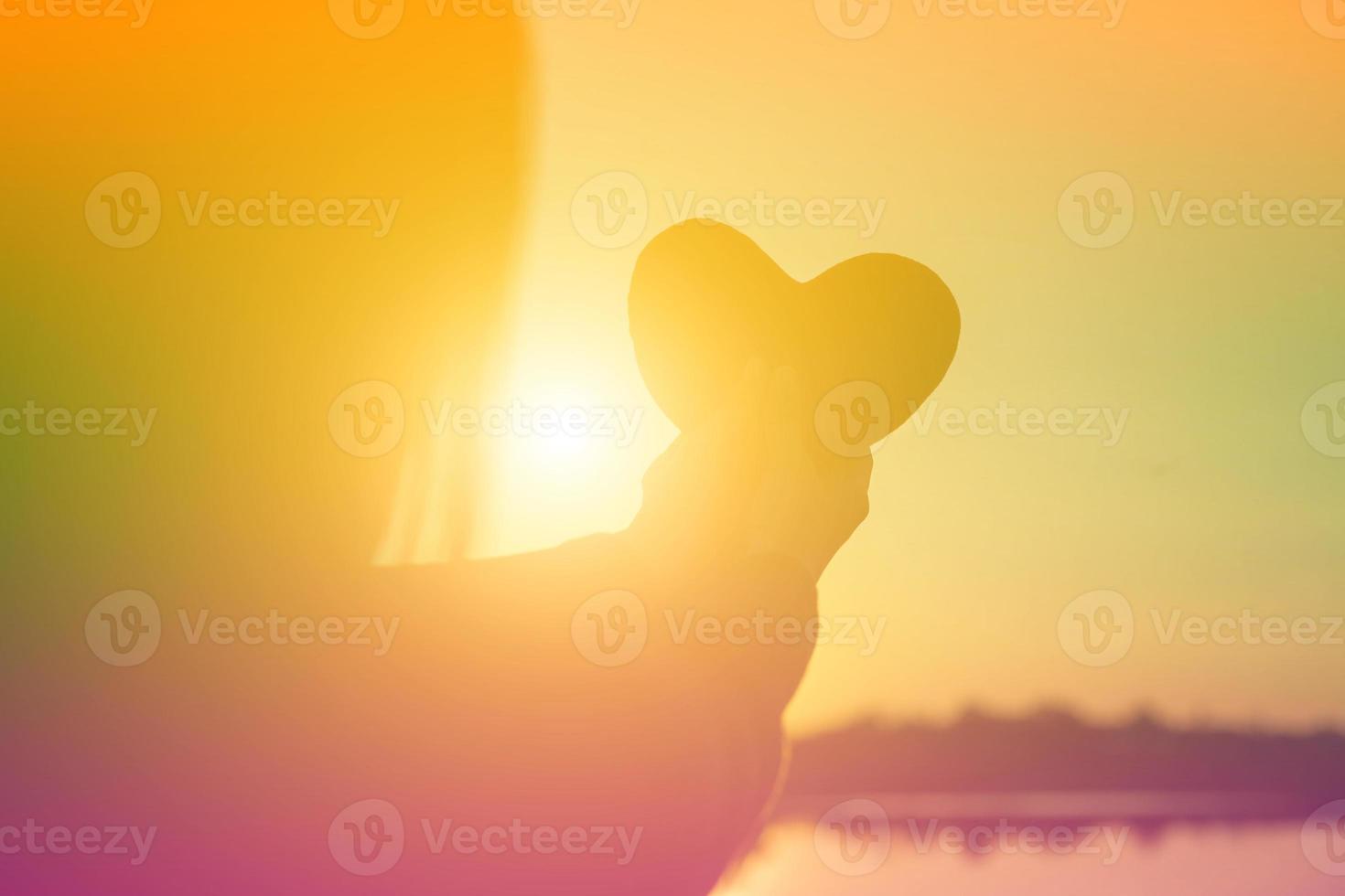 hands forming a heart shape with sunset silhouette photo