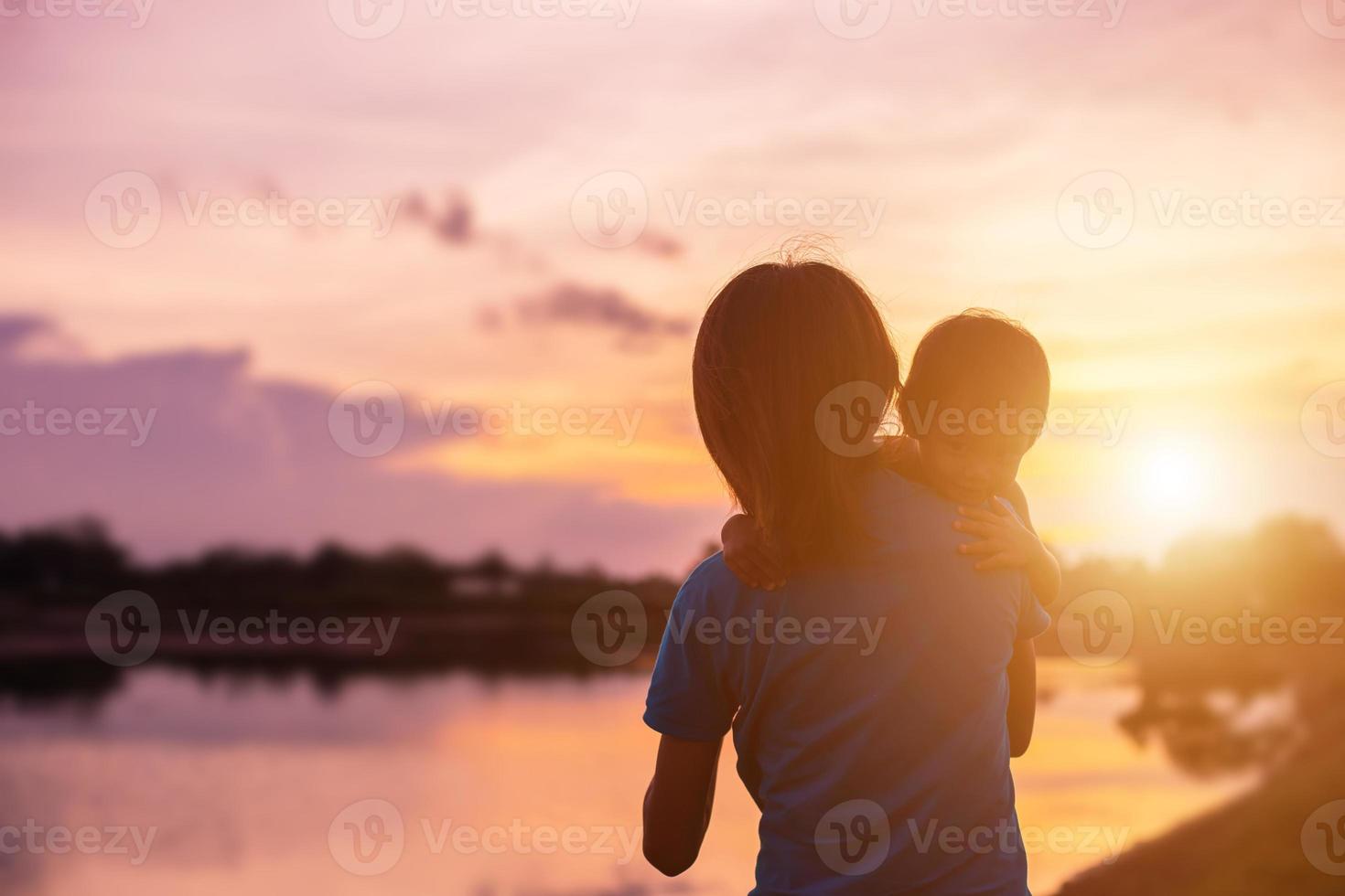 a silhouette of a happy young girl child the arms of his loving mother for a hug, in front of the sunset in the sky on a summer day. photo